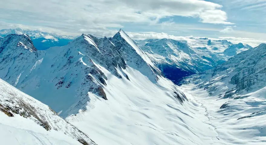 Vette innevate e un cielo azzurro con nuvole soffici, un panorama mozzafiato per chi cerca cosa vedere a Courmayeur.