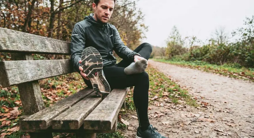 Runner seduto su una panchina controlla le sue scarpe da corsa, pensando a ogni quanto cambiarle per non incorrere in infortuni.