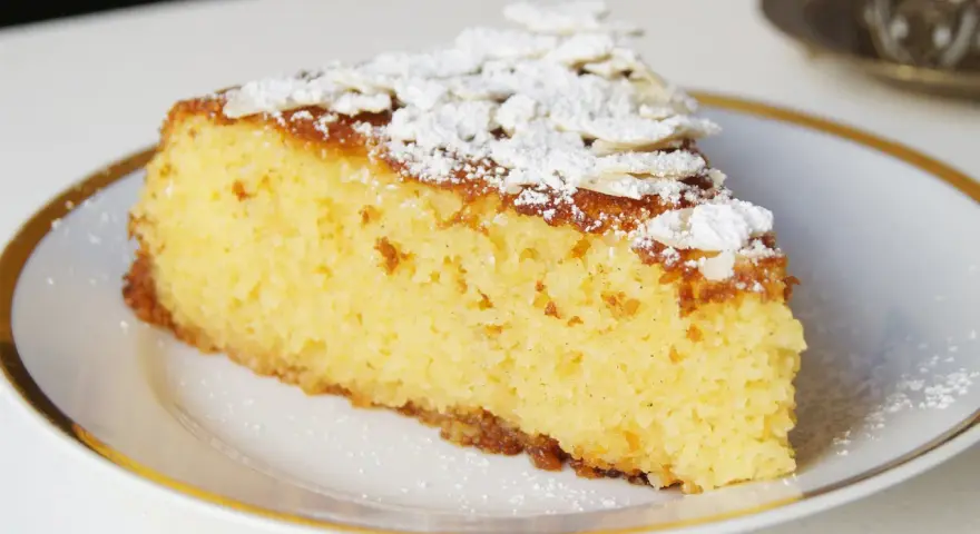Rebanada de tarta de almendra esponjosa, espolvoreada con azúcar glas y láminas de almendra.