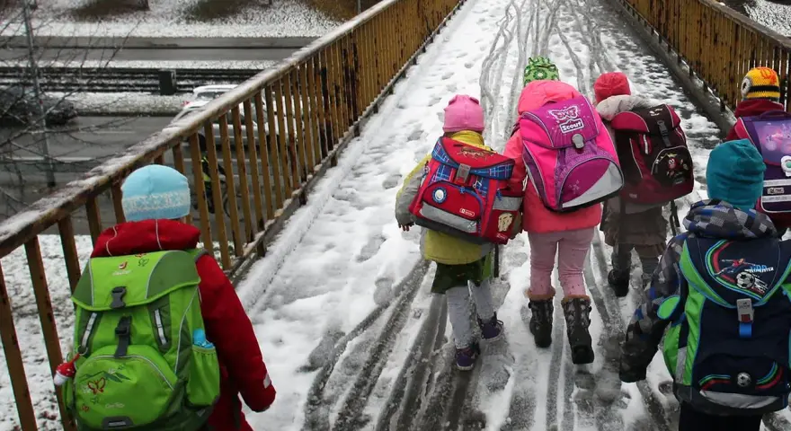 Kinder mit bunten Rucksäcken auf verschneiter Brücke, unterwegs zu den weihnachtsferien mv 2025.