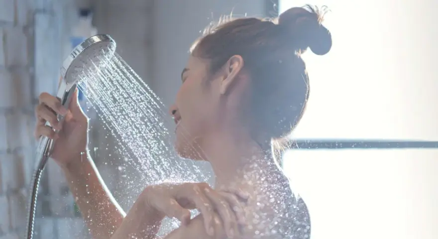 Donna sotto la doccia, l'acqua della doccia esce alternativamente calda e poi fredda, creando un effetto rinfrescante.