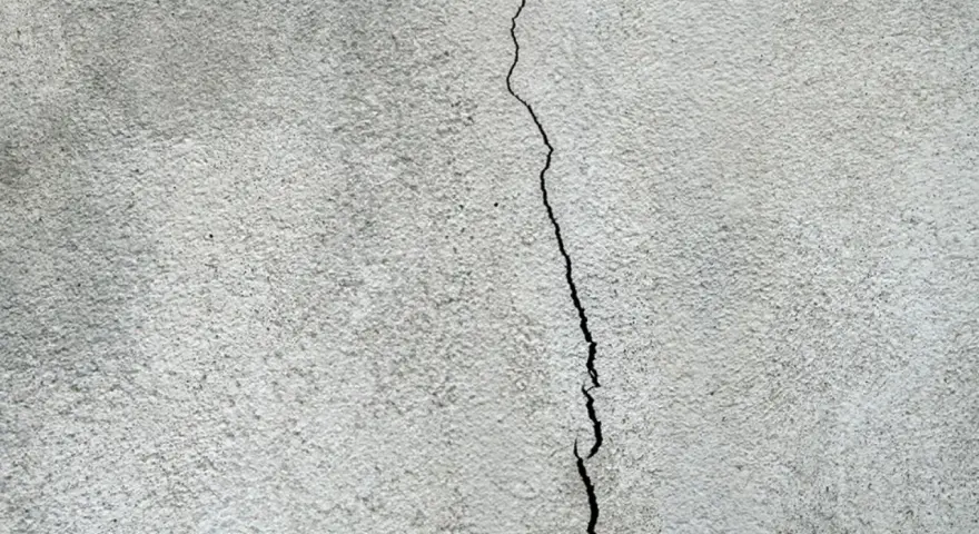 En spricka löper vertikalt över en grov, grå yta, som kan vara en husgrund som behöver putsa.