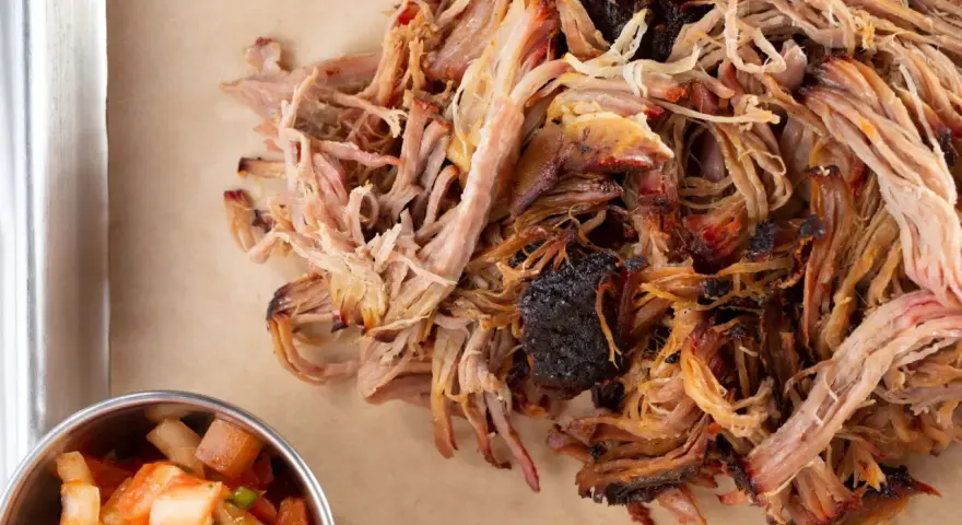 Zartes Pulled Pork, perfekt gegart, zeigt die ideale pulled pork kerntemperatur. Daneben eine Schale mit frischer Salsa.