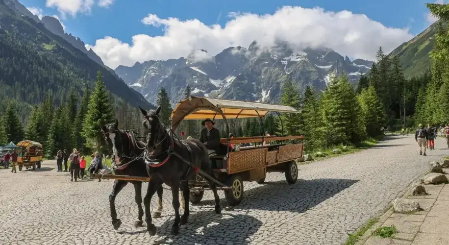 Konny zaprzęg na trasie do Morskiego Oka, z turystami w wozie i górami w tle.