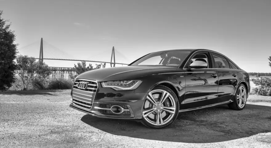 Elegancki czarny Audi S6 C7 z charakterystycznym grillem i felgami, zaparkowany na tle mostu wiszącego.