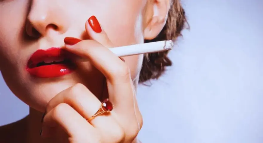 Labios rojos, uñas rojas y un cigarrillo. Una mujer se lleva el cigarrillo a la boca, quizás pensando que la nicotina adelgaza.