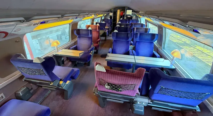 Interior of a bullet train, ready for a journey from Paris to Nice. Plush blue seats with tray tables line the carriage.