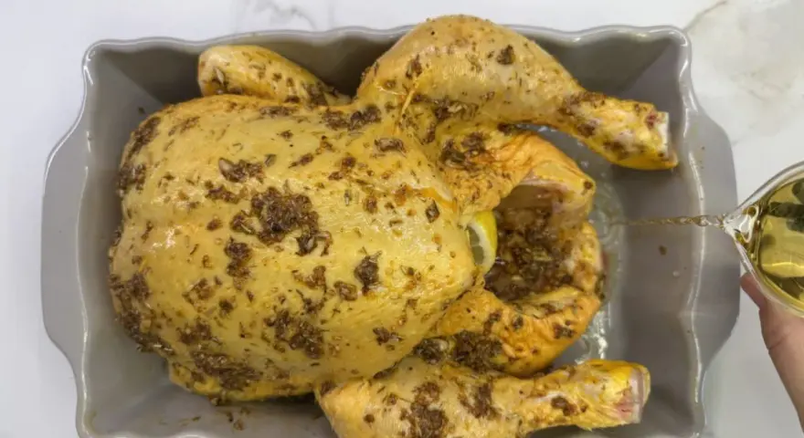 Un pollo al ast, sazonado y listo para hornear, recibe un chorrito de aceite para una cocción perfecta.