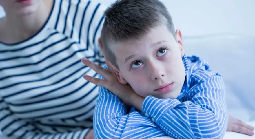 Bambino con sguardo pensieroso, forse durante un test autismo bambini 2 anni. La madre lo osserva con preoccupazione.