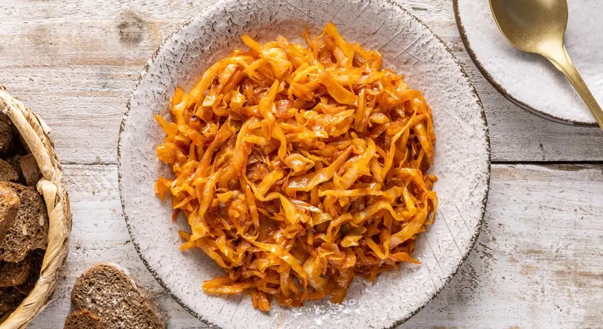 Un saporito cappuccio stufato in padella, servito in un piatto rustico, accompagnato da pane scuro e una posata dorata.