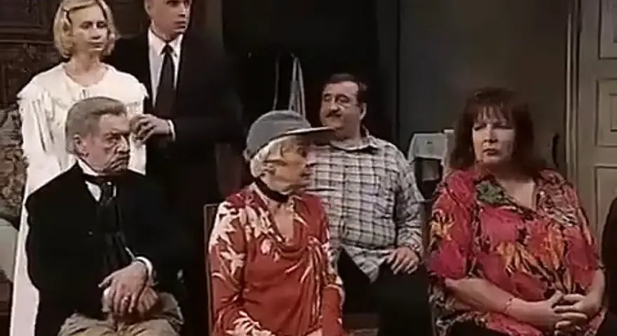 Scena z filmu "Tango" Mrożka. Grupa osób siedzi i stoi w pomieszczeniu.