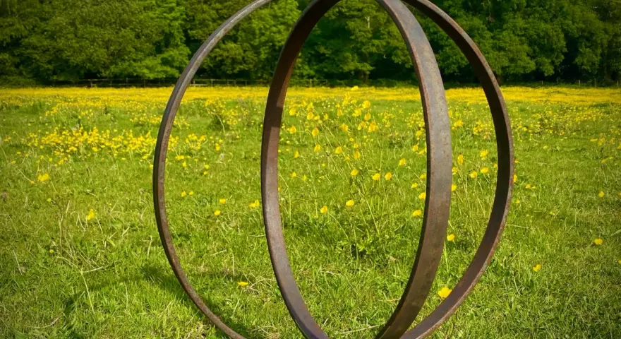 Metallskulptur im Feld mit gelben Blumen. Eine Idee, wie man ein Rondell im Garten gestalten kann, mit rustikalem Charme.