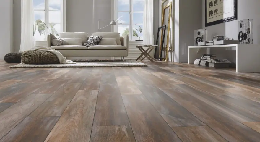 Sala de estar moderna con suelo de tarima AC5 de aspecto madera desgastada, sofá beige, alfombra y pufs.