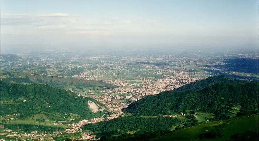 Vista panoramica dalla sella di Fadalto su una vasta pianura punteggiata di case e campi, con colline verdi in primo piano.