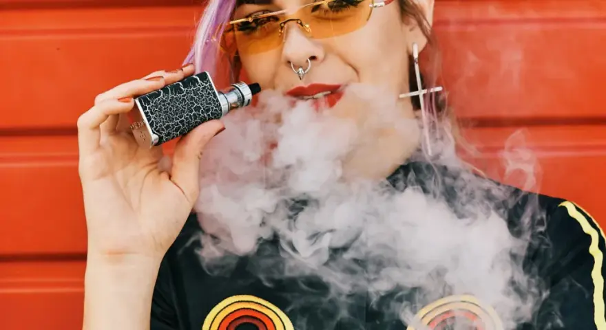 Joven con vaper exhala humo. ¿Cuántas calorías tiene un vaper? La respuesta es cero, ya que no contiene azúcares ni grasas.
