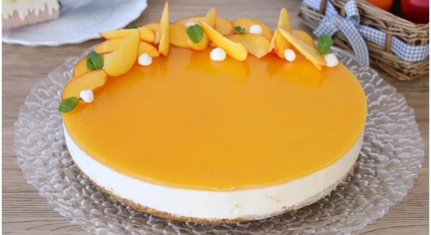 Delizioso cheesecake alle pesche con glassa lucida e fette di pesca fresca, guarnito con menta e piccole meringhe.