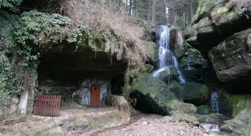 Ein versteckter Wasserfall bei Bad Schandau, mit einer kleinen Höhle und einer roten Tür.