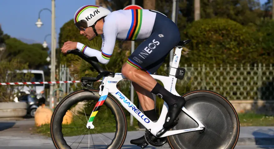 A cyclist in a rainbow jersey races a time trial bike, pushing hard during the Tour de France.