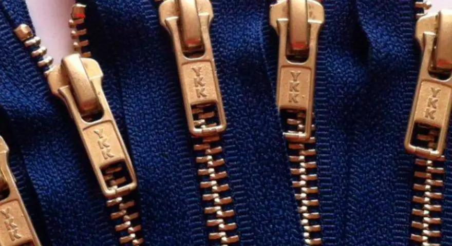 Primer plano de varias partes de una cremallera YKK dorada sobre tela azul.