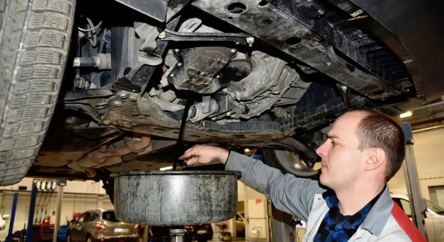 Mechanik spuszcza olej z silnika samochodu. Regularna wymiana oleju to klucz do długowieczności auta.