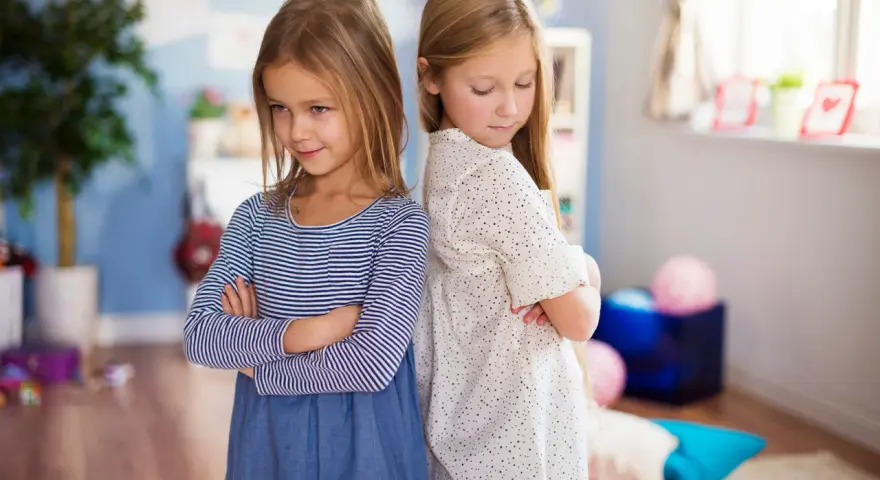 Dwie dziewczynki stoją plecami do siebie ze skrzyżowanymi rękami. W tle pokój dziecięcy. Jak nie zwariować ze swoim dzieckiem?