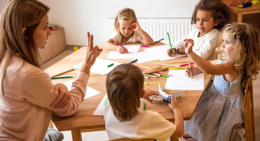Bambini disegnano e giocano con un aereo, guidati da un'insegnante. Un esempio di come le scienze della formazione sbocchi in attività creative e formative.
