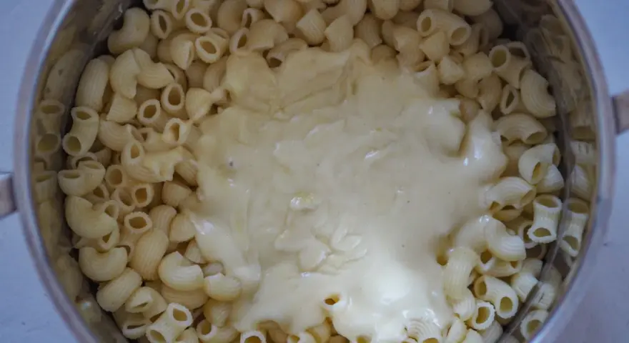 Gęsty, kremowy sos serowy otula makaron w garnku, tworząc pyszny makaron mac and cheese.