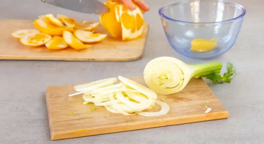 Frischer Fenchelsalat wird zubereitet. Eine Person schneidet Orangen, während Fenchelscheiben auf einem Holzbrett liegen.