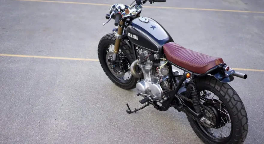 Klasyczny motocykl Yamaha z brązowym siedzeniem i gwiazdą na baku. Kraj pochodzenia tego modelu to Japonia.