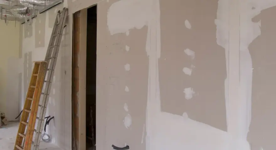 Scianka dzialowa z plyty kartonowo gipsowej w trakcie prac. Widoczne drabiny, instalacje i otwór drzwiowy.