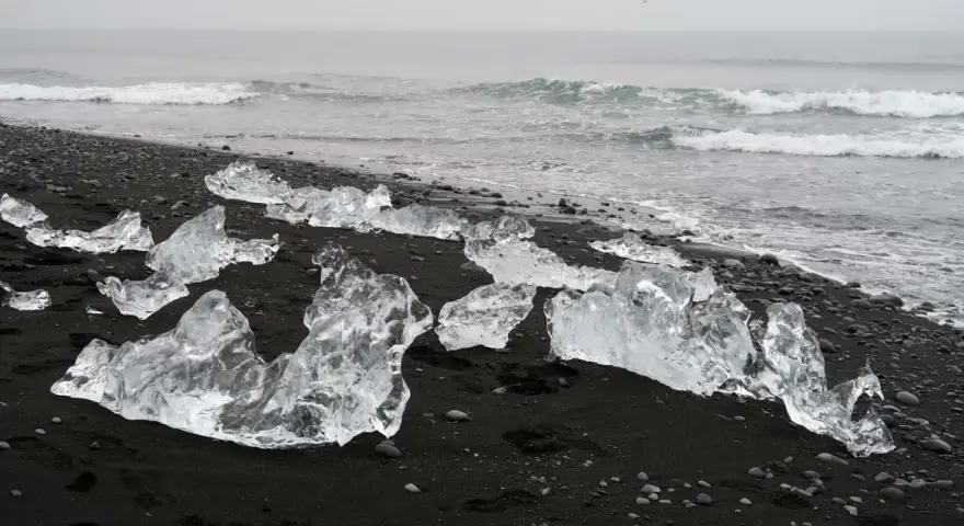 Lodowe bryły na czarnym piasku tworzą magiczną diamentową plażę Islandii. Fale oceanu delikatnie obmywają ten niezwykły krajobraz.