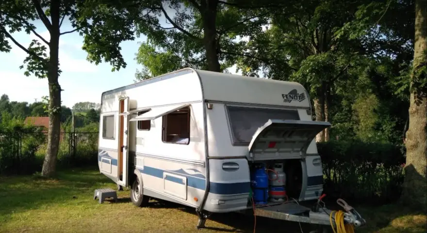 Przygotowania do wypoczynku na **camping Duszniki Zdrój**. Przyczepa kempingowa z otwartym bagażnikiem, w którym widać butle gazowe.