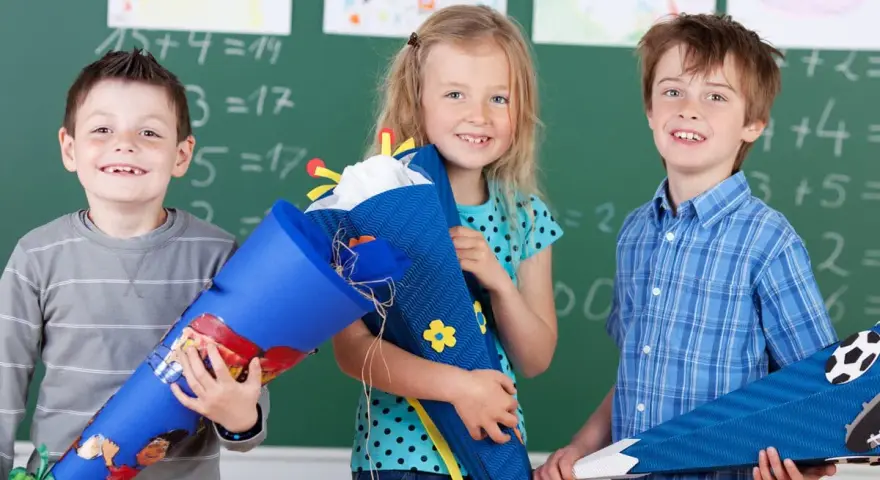 Drei Kinder mit Schultüten vor einer Tafel. Die Einschulung in Sachsen-Anhalt 2025 wird hier fröhlich gefeiert.