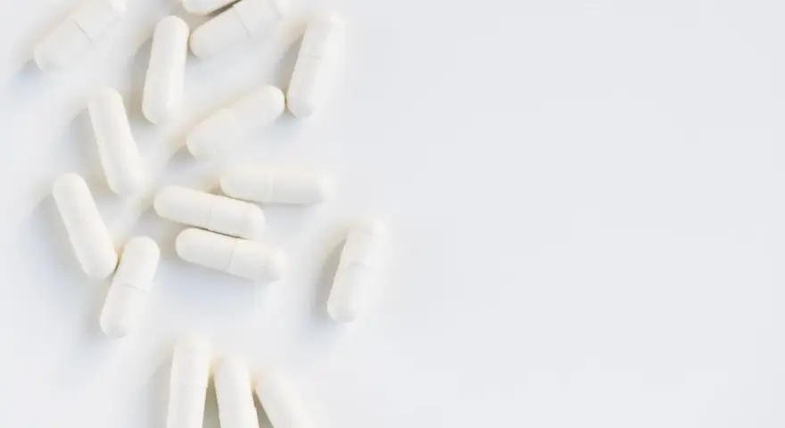 Vita kapslar utspridda på en vit yta. Kan dessa orsaka l-glutamin biverkningar?