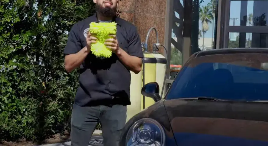 Man holding a fluffy wash mitt, ready to demonstrate how to wash a convertible car.