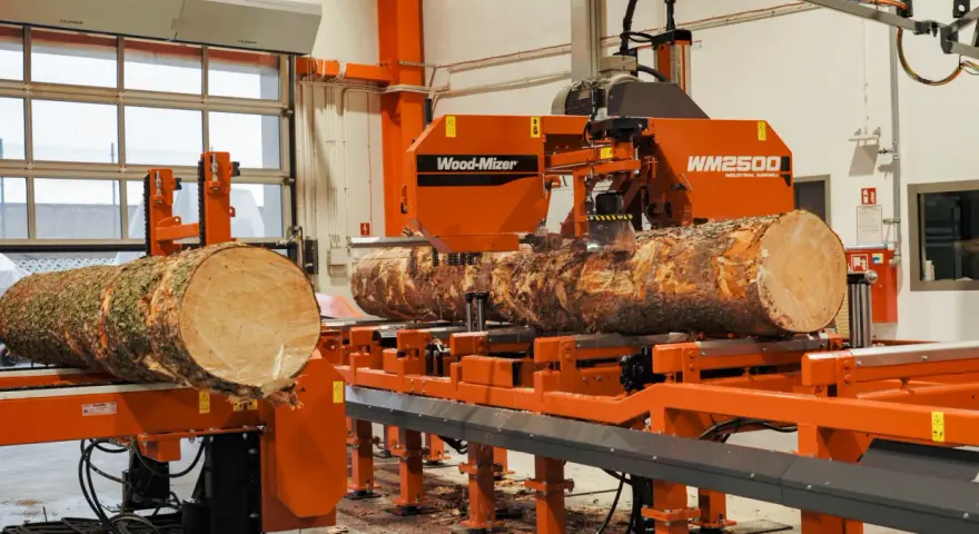 Pomarańczowa maszyna do obróbki drewna Wood-Mizer WM2500 przetwarza pień drzewa na deski.
