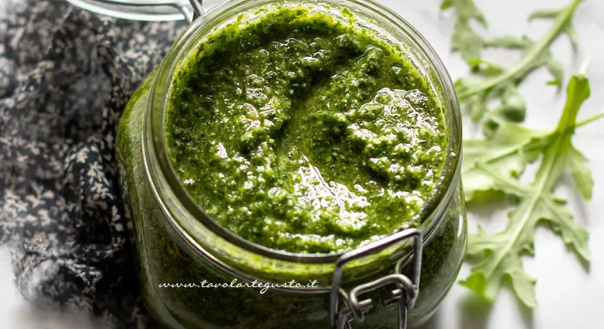 Un vasetto di pesto di rucola fatto in casa, con foglie di rucola fresca sullo sfondo.