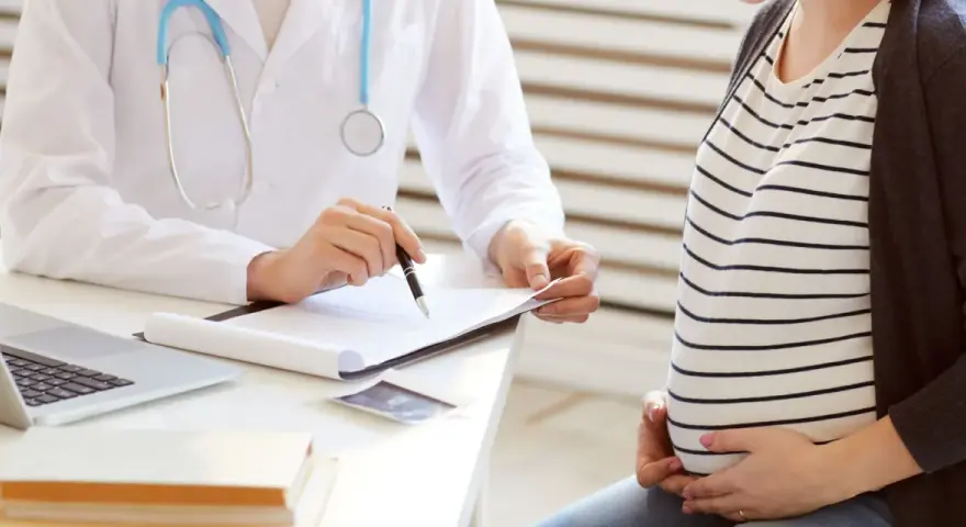 Lekarz omawia z ciężarną pacjentką kolejne trymestry ciąży, notując coś na dokumentach.
