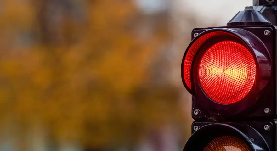 Close-up of a red traffic light with a blurred background of autumn foliage.