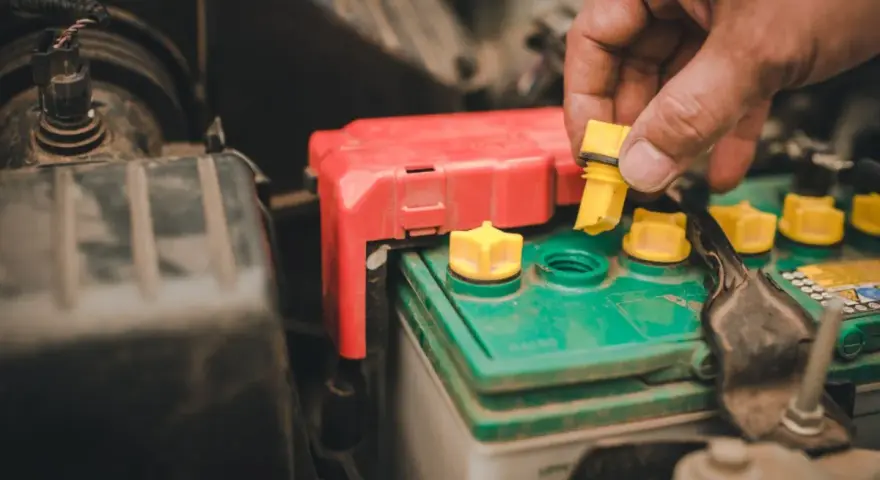 A hand removes a yellow cap from a truck battery, hinting at maintenance to ensure it lasts as long as possible.