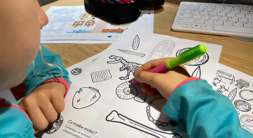 Dziecko koloruje edukacyjne karty pracy z dinozaurem i artefaktami.