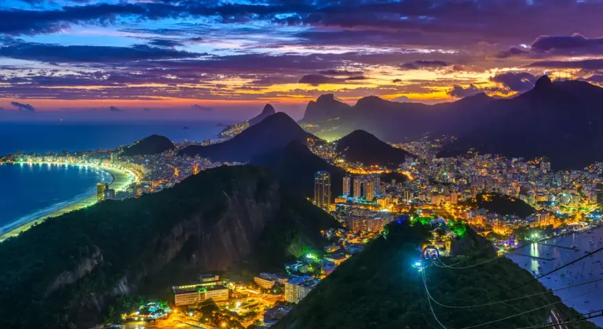 Zachód słońca nad słynną plażą w Rio de Janeiro. Miasto rozświetlone tysiącami świateł, góry i ocean tworzą magiczny widok.