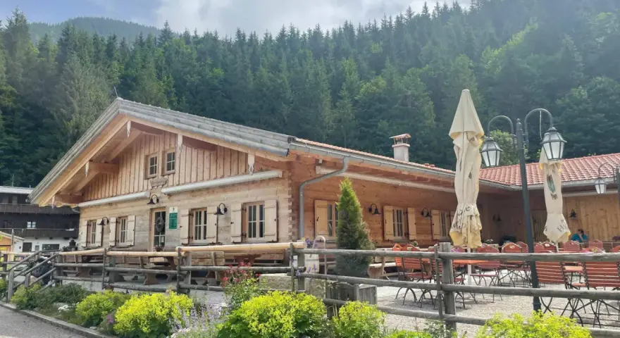 Holzhütte mit Biergarten und blühenden Blumen vor einer Bergkulisse. Die untere Firstalm lädt zum Verweilen ein.