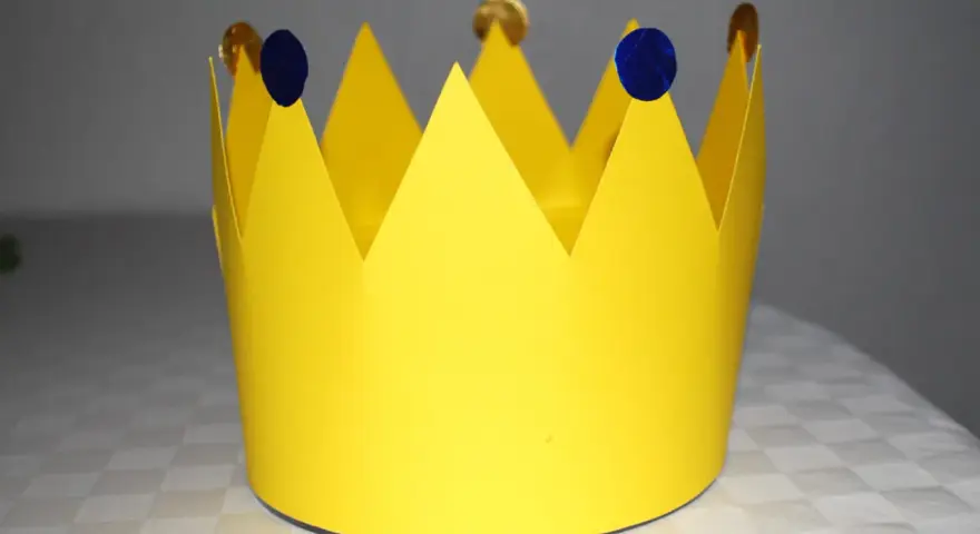 Gelbe Papierkrone, die zum **krone basteln** einlädt. Mit blauen Tupfern und goldenen Münzen verziert, wartet sie auf ihren kleinen König oder ihre kleine Königin.