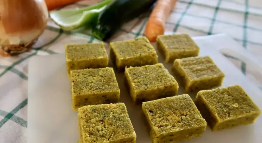 Cubetti di dado vegetale fatto in casa, pronti per insaporire le tue ricette. Sullo sfondo, ingredienti freschi come carote, zucchine e cipolla.