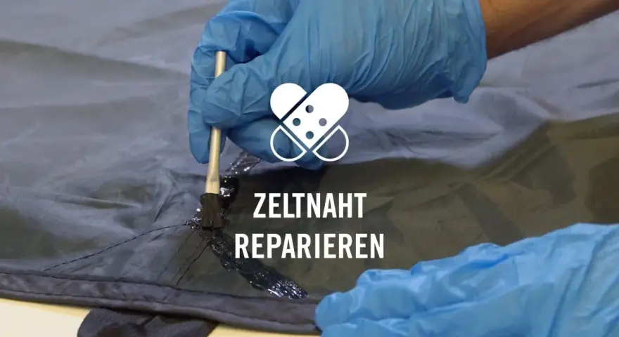 Mit einem Pinsel wird eine schwarze Dichtmasse auf eine Zeltnaht aufgetragen, um sie abzudichten und zu reparieren.