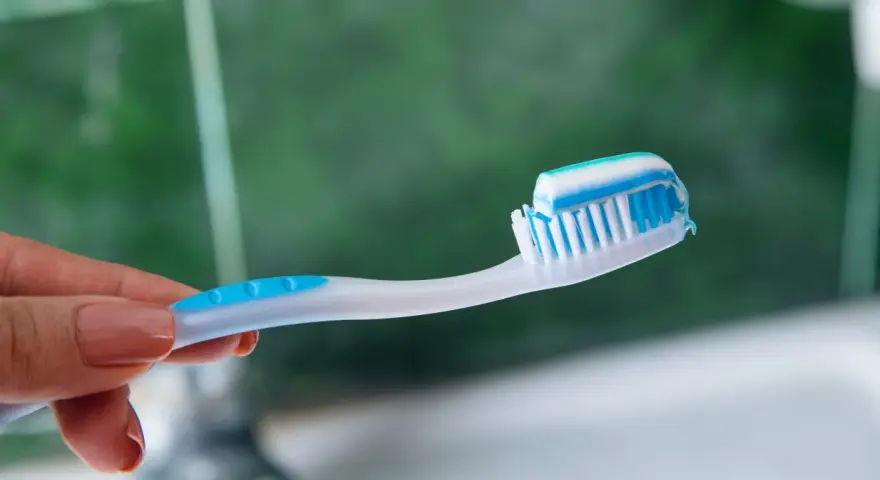 Dłoń trzymająca szczoteczkę z biało-niebieską pastą. Idealna jaka pasta po wybielaniu zębów dla lśniącego uśmiechu.