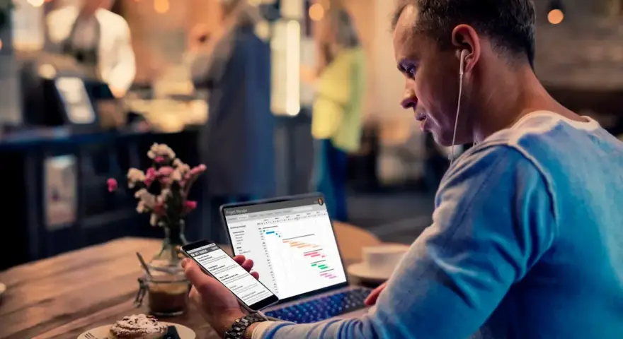 Hombre revisa datos de business intelligence hostelería en su laptop y móvil, sentado en una cafetería.