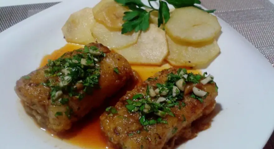 Dos trozos de bacalao a la llauna con patatas y perejil.