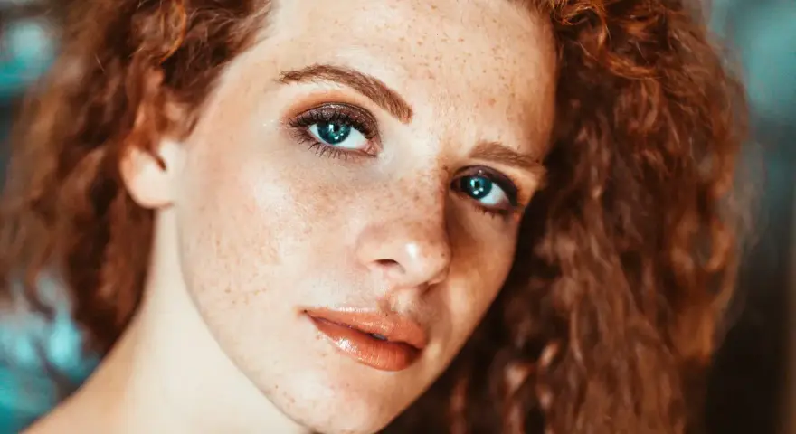 Primo piano di una ragazza con lentiggini e capelli rossi, con un trucco naturale che esalta la sua bellezza.